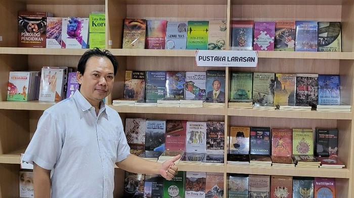 Slamat Trisila berpose di depan buku-buku yang diterbitkan melalui Pustaka Larasan. (Foto: Dok. Istimewa)