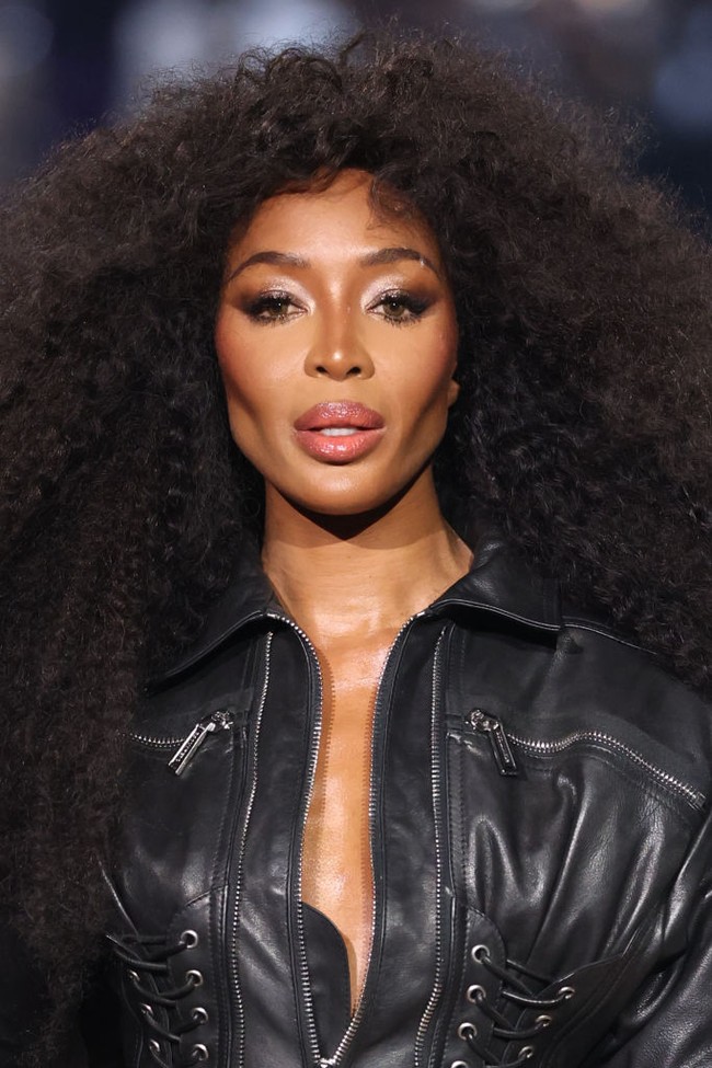 Untuk makeup, Naomi tampil dengan smokey eyes bernuansa cokelat yang tajam, serta contouring di pipi yang menonjolkan struktur wajahnya. Look ini semakin memperkuat aura fierce yang khas dari seorang supermodel asal Inggris ini. Foto: Getty Images/Estrop