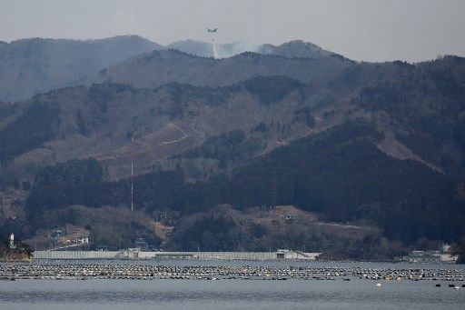 A Japan Self-Defense Force aircraft (top C) sprays water over hilltops as officials continue to fight a wildfire near the city of Ofunato, Iwate Prefecture on February 28, 2025. Military helicopters have been mobilised to try and douse the flames raging in forested areas of Ofunato in the northern region of Iwate. (Photo by JIJI Press / AFP) / Japan OUT