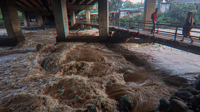 Pengendara melintas di jembatan dengan latar Sungai Ciliwung yang meluap di Ciawi, Kabupaten Bogor, Jawa Barat, Senin (3/3/2025). Hujan deras yang melanda kawasan Puncak, Bogor, mengakibatkan debit Sungai Ciliwung meluap dan Bendung Katulampa mencatat Tinggi Muka Air (TMA) Sungai Ciliwung setinggi di 200 centimeter atau saga satu Minggu malam (2/3/2025) pukul 21.20 WIB. ANTARA FOTO/Yulius Satria Wijaya/YU