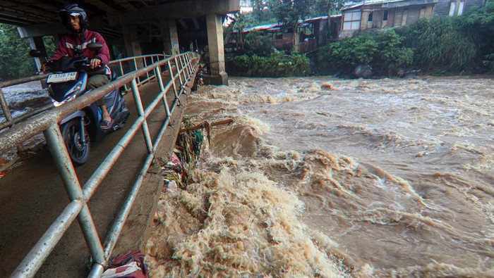 Pengendara melintas di jembatan dengan latar Sungai Ciliwung yang meluap di Ciawi, Kabupaten Bogor, Jawa Barat, Senin (3/3/2025). Hujan deras yang melanda kawasan Puncak, Bogor, mengakibatkan debit Sungai Ciliwung meluap dan Bendung Katulampa mencatat Tinggi Muka Air (TMA) Sungai Ciliwung setinggi di 200 centimeter atau saga satu Minggu malam (2/3/2025) pukul 21.20 WIB. ANTARA FOTO/Yulius Satria Wijaya/YU