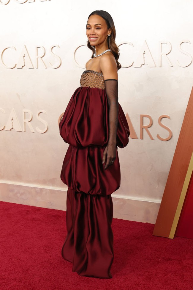 Bagian bustier transparan pada gaun Zoe Saldana ini disatukan dengan tiga lapis keliman gelembung atau bubble berwarna burgundy. Zoe menambah glamor gayanya dengan mengenakan sarung tangan opera hitam transparan. Foto: Getty Images/Mike Coppola