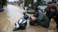 Seorang warga mendorong sepeda motornya yang mogok akibat banjir. 