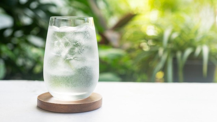 A refreshing glass of ice water on bright green morning light background.