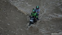 Ojek online membonceng penumpang melewati banjir di Bekasi, Selasa (4/3/2025).