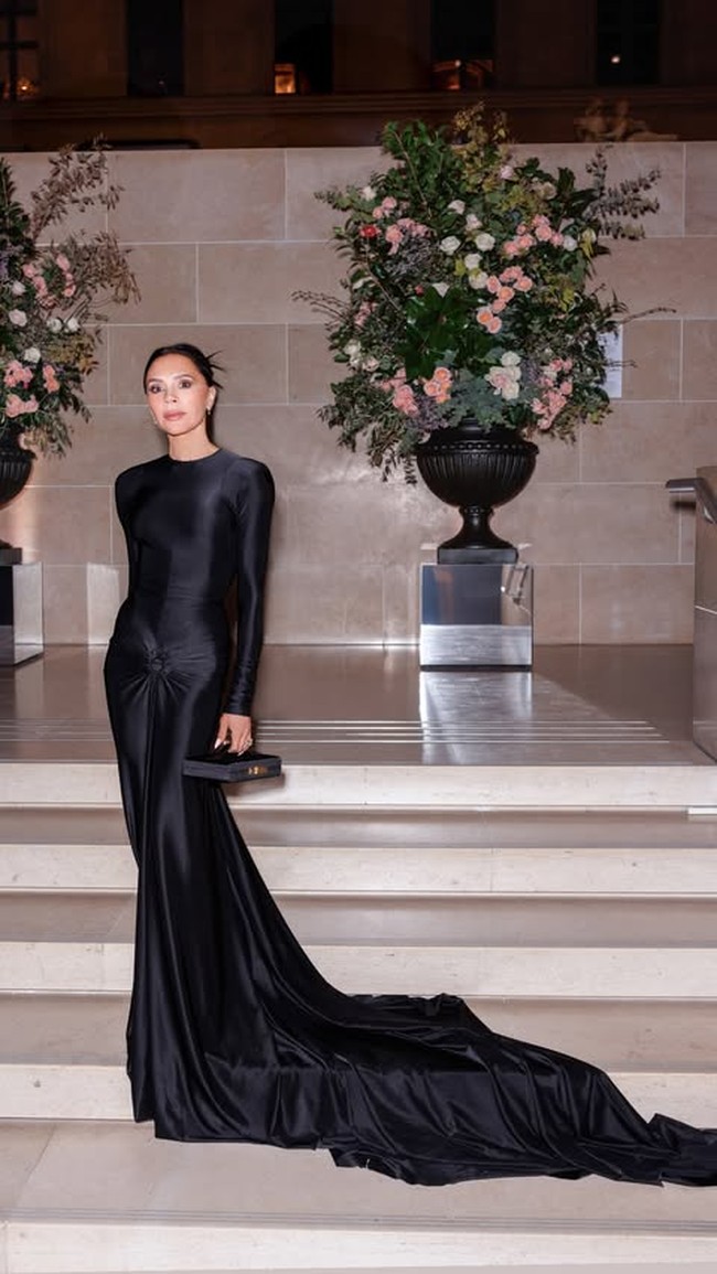 Sesuai dengan tema acara, pasangan yang memiliki empat orang anak tersebut tampil dengan elegansi. Dalam foto yang dibagikan di Instagram, Victoria terlihat memilih gaun hitam dengan lengan juga ekor yang panjang dan membentuk badan. Dalam acara fashion tersebut, Victoria terlihat menawan dengan riasan rambut cepol dan anting kecil. Foto: Instagram Victoria Beckham