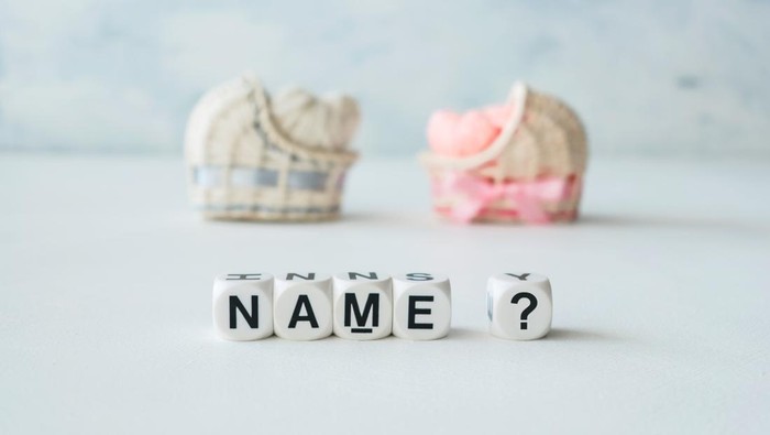 Concept of choosing baby name. Pink and blue decorative straw cradles with thread hearts and text name? on light background