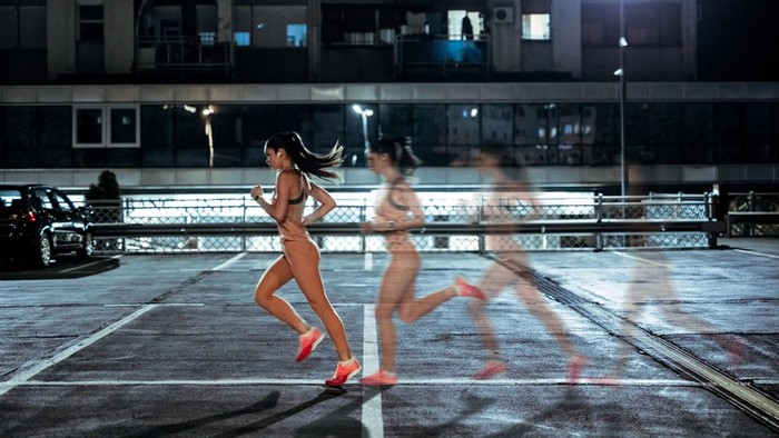 Young beautiful athlete Caucasian woman running in public garage at night. Photo manipulation.
