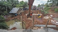 Pekerja merapikan tiang penyangga jembatan darurat menggunakan alat berat di Jalan Lintas Sumatera yang amblas, Desa Sirih Sekapur, Bungo, Jambi, Kamis (6/3/2025).  