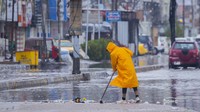 Seorang pekerja kota membersihkan air hujan dari jalan-jalan yang banjir di Kota Sadr setelah hujan lebat.