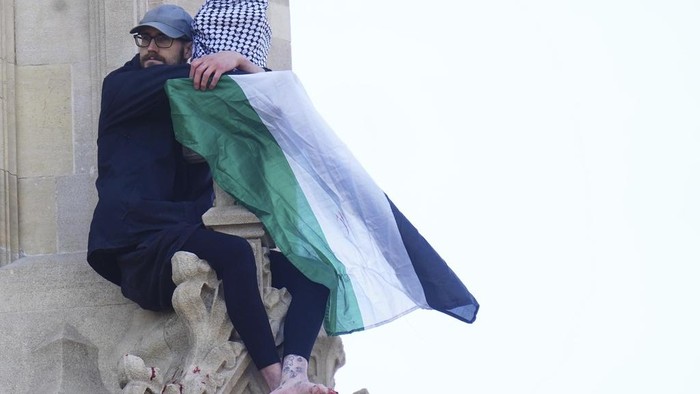Aksi Pria Kibarkan Bendera Palestina di Big Ben London, Berakhir Ditangkap A man with a Palestinian flag clings to the structure after he climbed up Elizabeth Tower, which houses Big Ben at the Palace of Westminster in London. Saturday, March 8, 2025. (James Manning/PA via AP)