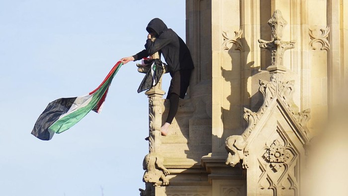 A man with a Palestinian flag clings to the structure after he climbed up Elizabeth Tower, which houses Big Ben at the Palace of Westminster in London. Saturday, March 8, 2025. (James Manning/PA via AP)