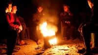 Warga Palestina duduk di sekitar api unggun sementara seorang pria berdiri di toko darurat selama pemadaman listrik, di Rafah di Jalur Gaza selatan, 9 Maret 2025.  