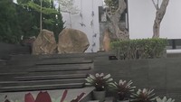 Halaman samping rumah tampak lebih tinggi dan disertai tangga. Area itu dihias dengan batu-batu besar, pohon, semak, serta tanaman pot. Foto: Septian Bima Bagaskara