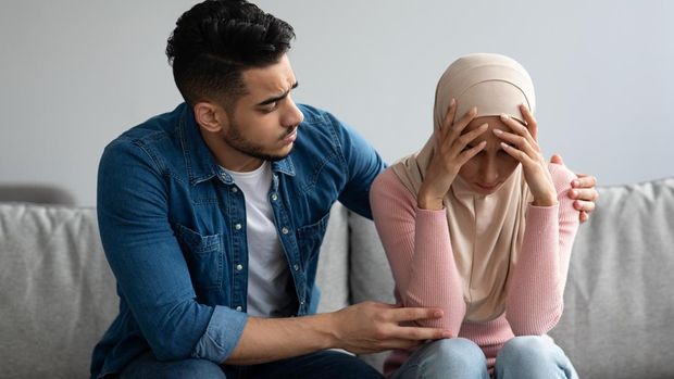 Middle-eastern bearded man comforting his crying wife, young muslim couple having problems in relationships, visiting family therapist together. Frustrated lady in hijab feeling unhappy