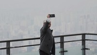 Seorang pria mengambil gambar saat pemandangan kota ditutupi kabut tebal berupa partikel debu halus di Gunung Namsan di Seoul, Korea Selatan, Rabu (12/3/2025). Pemerintah kota Seoul menerapkan protokol darurat untuk mengurangi polutan debu halus pada musim semi tahun ini.