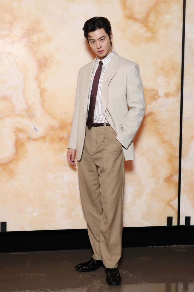 Tahun ini, Cha Eun Woo menampilkan office attire look di peragaan busana Saint Laurent. Bintang drama Korea True Beauty itu memadukan setelan jas berwarna krem, celana panjang senada, kemeja garis-garis, dan dasi berwarna burgundy. Foto: dok. Getty Images