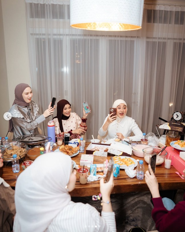 Margin Wieheerm tampil clean dengan pilihan cardigan putih berkerah, dengan detail kancing emas dan rok satin berwarna abu-abu terang. Sedangkan Aurel Hermansyah yang berdiri di sampingnya memadukan blus satin bernuansa ivory dan merah maroon, celana tabrak motif, dan pashmina menjuntai dengan gaya meleyot. Foto: dok. Instagram @kesharatuliu05, dok. Instagram @marginw