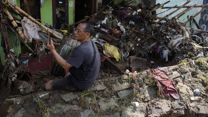 Warga menggunakan gawai di depan rumah yang rusak terdampak banjir akibat tanggul Sungai Cigede jebol di Desa Citeureup, Kabupaten Bandung, Jawa Barat, Minggu (16/3/2025). Puluhan rumah mengalami kerusakan serta ratusan kepala keluarga terdampak banjir akibat tanggul Sungai Cigede sepanjang 30 meter jebol saat hujan dengan intensitas tinggi pada Sabtu (15/5) malam. ANTARA FOTO/Novrian Arbi/tom.