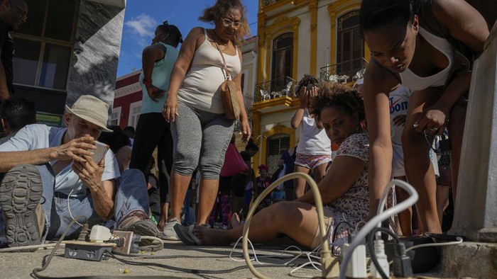 Warga Kuba Ramai-ramai Charge HP Saat Pemadaman Listrik Massal Residents charge their electronic devices on a street during a general blackout in Havana, Saturday, March 15, 2025. (AP Photo/Ramon Espinosa)