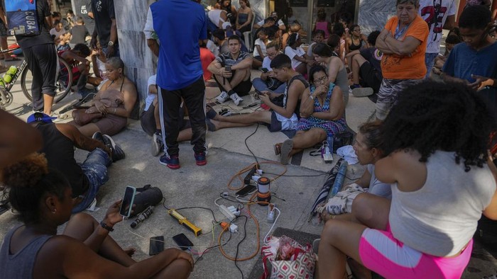 Residents charge their electronic devices on a street during a general blackout in Havana, Saturday, March 15, 2025. (AP Photo/Ramon Espinosa)