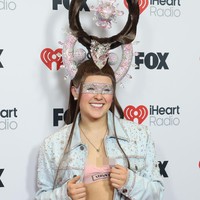 Wanita 21 tahun ini tampil heboh dengan wig cokelat panjang yang disanggul tinggi membentuk struktur melingkar, lengkap dengan hiasan bundar berkilauan warna pink yang menggantung di tengahnya. Foto: Christopher Polk/Variety via Getty Images