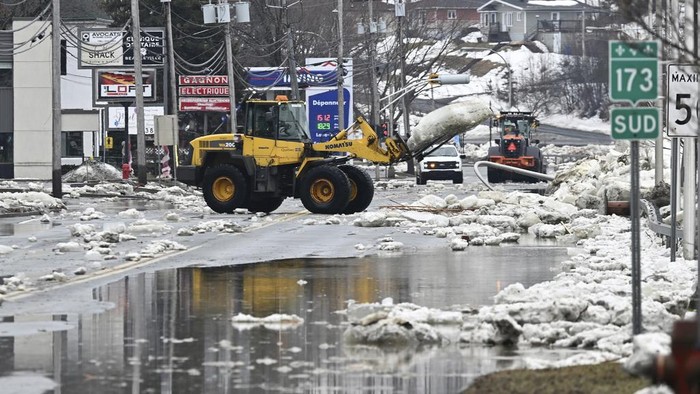 An excavator carries a block of ice caused by flooding from the Chaudiere river on a roadway in Beauceville, Quebec, Monday, March 17, 2025. (Jacques Boissinot/The Canadian Press via AP)
