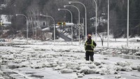 Seorang petugas pemadam kebakaran berdiri di tengah bongkahan es di jalan raya dari sungai Chaudiere di Beauceville, Quebec, Kanada, Senin (17/3/2025).