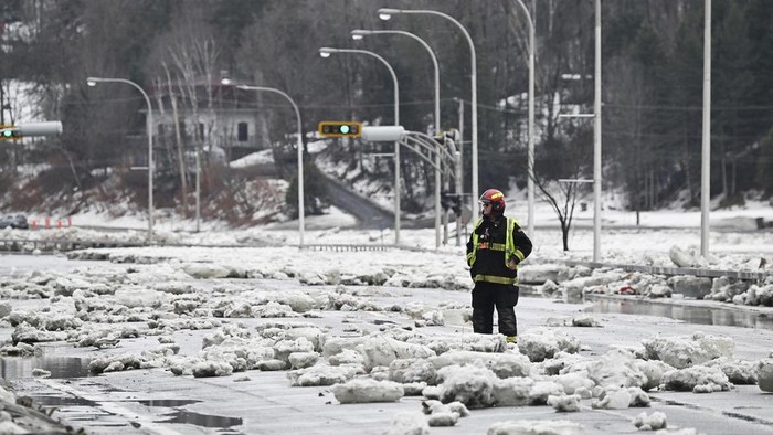 An excavator carries a block of ice caused by flooding from the Chaudiere river on a roadway in Beauceville, Quebec, Monday, March 17, 2025. (Jacques Boissinot/The Canadian Press via AP)