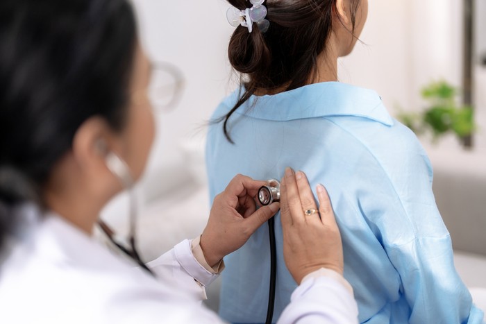 Doctor uses stethoscope to listen to the lungs of a female Asian patient to determine symptoms and provide treatment.