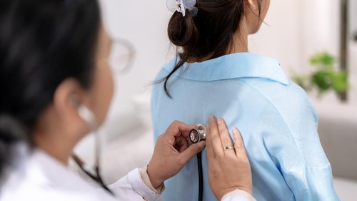 Doctor uses stethoscope to listen to the lungs of a female Asian patient to determine symptoms and provide treatment.