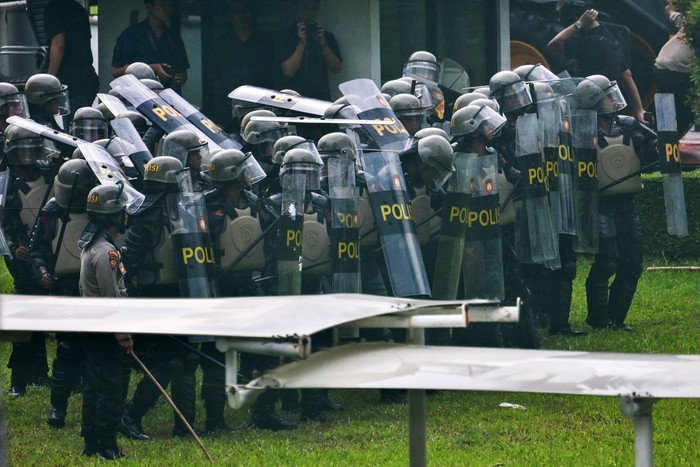 Anti-riot police shield up as students throw stones during a demonstration against a revision to the armed forces law in front of the House of Representatives building in Jakarta on March 20, 2025. Indonesias parliament on March 20 amended a law to allow members of the military to hold more government roles, despite criticisms it would expand the armed forces role in civilian affairs. (Photo by BAY ISMOYO / AFP)