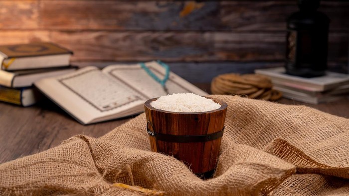 Holy Quran and a grain of rice in a wooden bowl in the sack on a wooden table, Islamic zakat concept. Muslims to help the poor and needy. Conceptual shoot for property, income, and fitrah zakat.