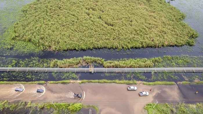 Foto udara kendaraan melintasi jalan yang terendam banjir di Betara 10, Tanjung Jabung Barat, Jambi, Sabtu (22/3/2025). Banjir yang disebabkan luapan Sungai Pengabuan tersebut mengakibatkan akses jalan dari Tanjung Jabung Barat bagian hilir menuju sejumlah desa di bagian hulu terganggu, pengendara sepeda motor terpaksa menggunakan mobil bak terbuka dan truk untuk menyeberang dengan tarif Rp20 ribu. ANTARA FOTO/Wahdi Septiawan/Spt.