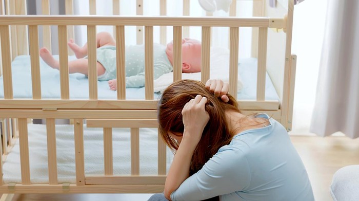 asian mother taking care her baby without patience sitting floor at home has postpartum depression and crying infant is lying on crib