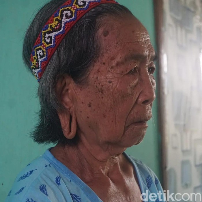 Di Desa Sungai Urang, Kabupaten Bulungan, Kalimantan Utara, sebuah rumah adat berdiri sederhana di tepi jalanan berbatu. Di samping bangunan tersebut, Lem Dungau, seorang nenek duduk dengan tenang.