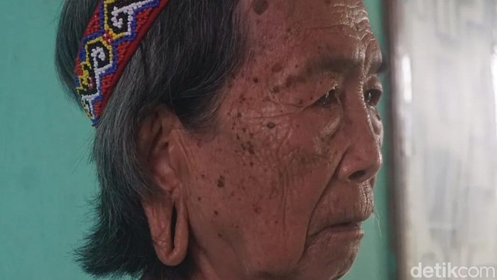 Di Desa Sungai Urang, Kabupaten Bulungan, Kalimantan Utara, sebuah rumah adat berdiri sederhana di tepi jalanan berbatu. Di samping bangunan tersebut, Lem Dungau, seorang nenek duduk dengan tenang.