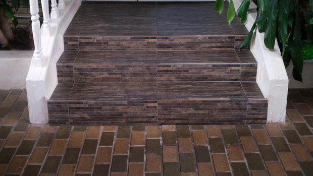 Brown tiled steps leading to a white door with white railing and green plants. Outdoor architecture photography