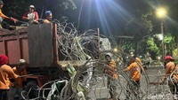 Petugas kebersihan bersama aparat polisi membersihkan kawat berduri usai demonstrasi di depan Gedung Negara Grahadi.