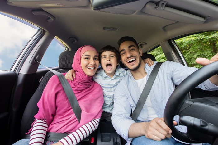 Road Fun. Joyful Muslim Family Of Three Singing Inside Of Car Together, Happy Middle Eastern Dad, Little Son And Mother In Hijab Enjoying Drive Trip Together, Laughing And Looking At Camera, Closeup