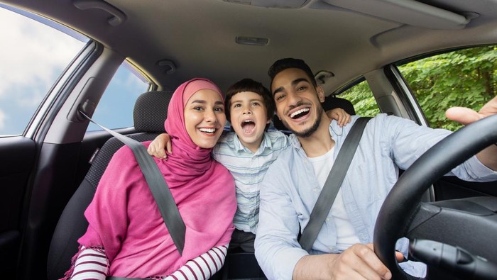 Ilustrasi mudik Lebaran Road Fun. Joyful Muslim Family Of Three Singing Inside Of Car Together, Happy Middle Eastern Dad, Little Son And Mother In Hijab Enjoying Drive Trip Together, Laughing And Looking At Camera, Closeup