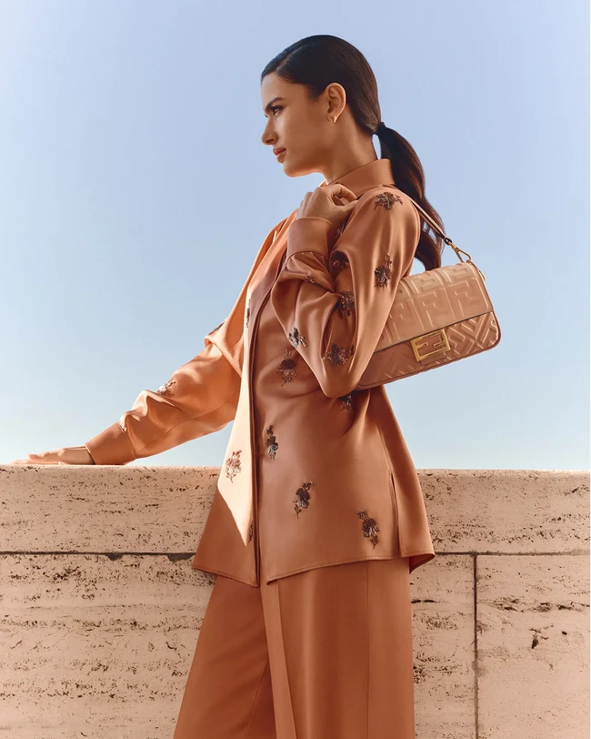 Fendi Noor Capsule Collection merayakan Ramadan dengan sentuhan sutra dan kilau emas, menghadirkan nuansa lembut peach dan terracotta yang terinspirasi dari keindahan gurun. Yas ikonis seperti Baguette, Peekaboo ISeeU Petite, dan Mini Fendigraphy, mendapat wajah baru dengan gradasi kulit pink yang elegan, mencerminkan cahaya matahari senja di atas bukit pasir. Mini Baguette, dihiasi sulaman payet bunga metalik dan gesper kristal pink yang memancarkan kemewahan tanpa perlu banyak kata. (Foto: Dok. Fendi)