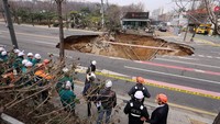 Petugas penyelamat berjalan melewati sinkhole yang muncul di jalanan kota Seoul, Korea Selatan, Selasa (25/5/2025). Lubang besar itu terbentuk di persimpangan di tenggara ibu kota Korea Selatan selama jam sibuk sore sekitar pukul 18.30 (09.00 GMT) pada 24 Maret. (REUTERS/Yonhap News Agency)