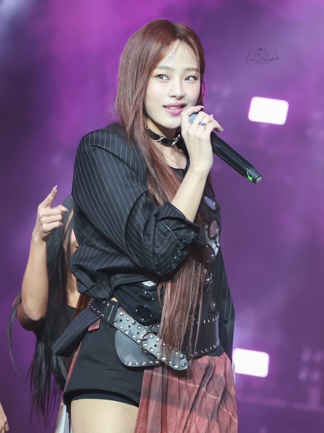 Personel tertua NJZ, Minji memamerkan kemampuan vokal dan rap saat menyanyikan lagu Smile For The Camera dari Upsahl. Dia membuat penggemar pangling dengan warna rambut coklat terang. Tampil memakai t-shirt dan blazer hitam berhias pin, pleated skirt merah bermotif kotak-kotak, dan knee high boots bulu-bulu berwarna abu-abu. Foto: dok. Twitter @EL_XLife