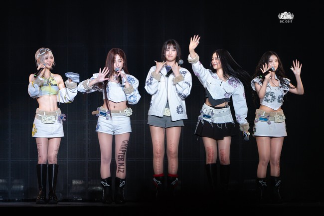 Untuk menutup penampilannya sebelum memutuskan hiatus, NJZ membawakan lagu baru mereka yang bertajuk PIT STOP. Minji, Hanni, Danielle, Haerin, dan Hyein mengenakan busana putih yang dirancang khusus oleh Denim Tears, dilengkapi aksesori phone belts ala Y2K. Beberapa personelnya juga memakai stocking transparan bertuliskan ‘Chapter NJZ’ dan ‘Unpredictable’. Foto: dok. Twitter @sc_0617