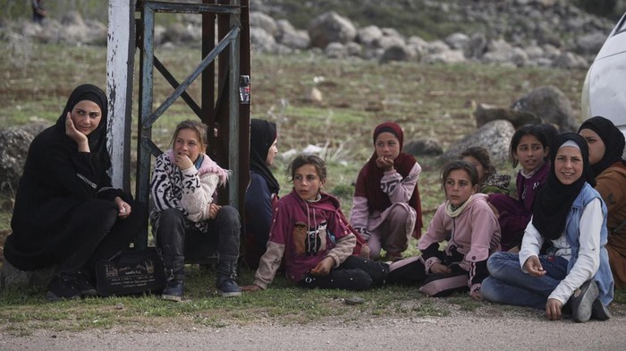 Local residents wait on the side of the road to be evacuated due to fears of Israeli army incursions, following a drone attack that reportedly killed at least four people in the area, on the outskirts of the village of Koayiah, southwestern Syria, Tuesday, March 25, 2025. (AP Photo/Omar Albam)