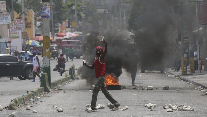 A local gestures on a street blocked by burning tires and debris during a demonstration demanding the resignation of the transitional presidential council, in Port-au-Prince, Haiti, Wednesday, March 26, 2025. (AP Photo/Odelyn Joseph)