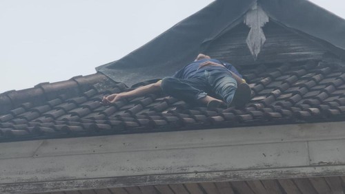 Seorang pria, T, yang tertidur di gnting rumah warga di Denpasar Timur, Rabu (26/3/2025) siang. Sebelumnya, T dikejar warga karena mencurigakan.