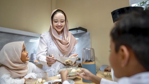 Indonesian Muslim wife serving ketupat rice dumpling for family in the house. Traditional Muslim food during the celebration of Happy Lebaran, Eid Al Fitr, Idul Fitri, and Ramadan Mubarak celebration