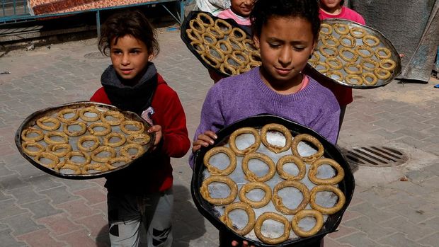 Anak-anak Palestina yang mengungsi memegang nampan saat mereka menyiapkan manisan tradisional untuk hari raya Idul Fitri yang menandai berakhirnya bulan puasa Ramadan, di Khan Younis di Jalur Gaza selatan pada 29 Maret 2025. (REUTERS/Hatem Khaled)